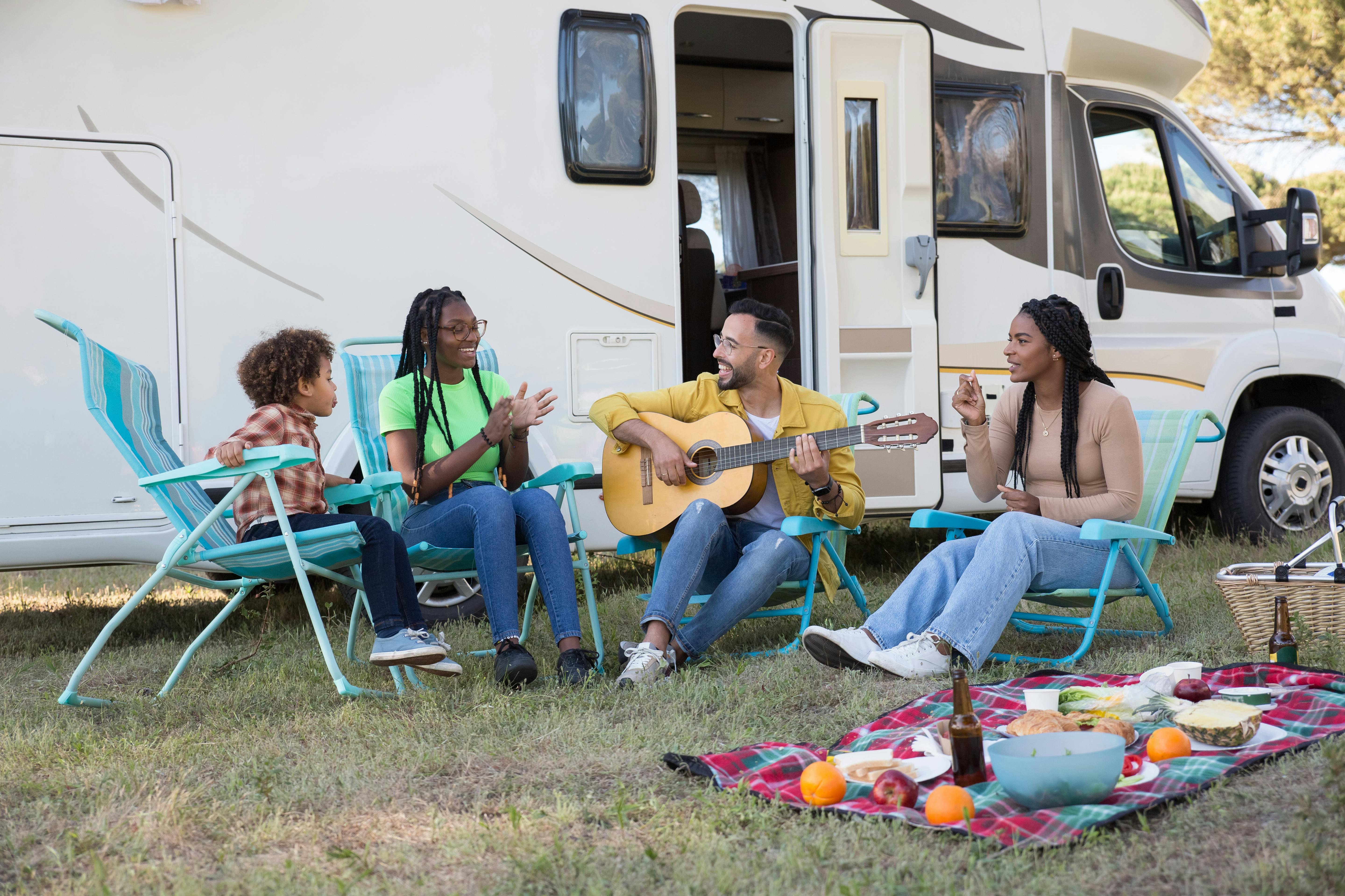 A family sitting in front of their RV in lawn chairs and singing.